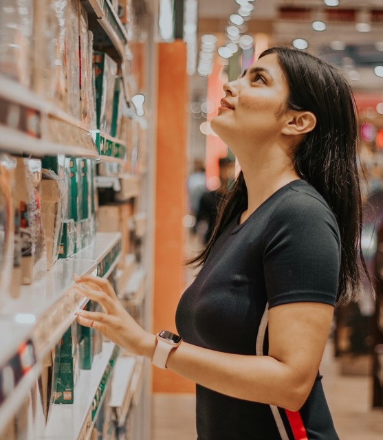 Shopalong fieldwork: a shopper weighing a purchase in a store aisle, her hand on a box, her eyes on the top shelf